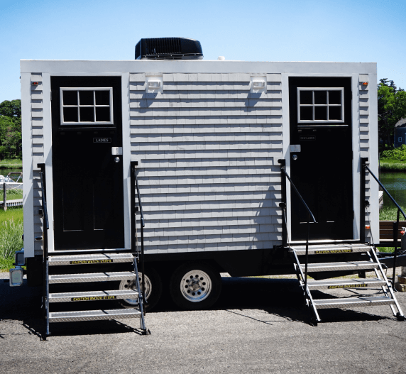 White and gray portable restroom trailer with two separate entrances and staircases.
