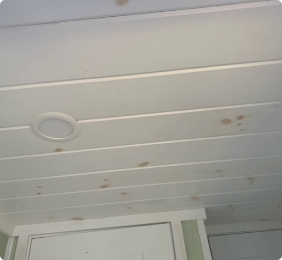 White paneled ceiling with recessed light, brown stains, and glimpse of a doorway.