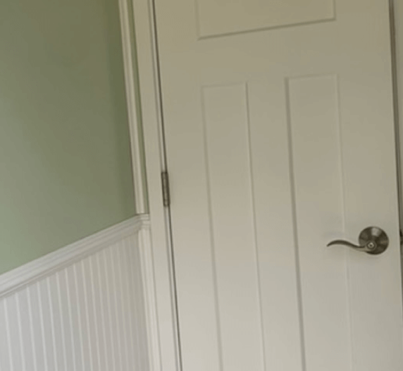 White door with three vertical panels, silver handle, next to a beadboard wall and green wall.