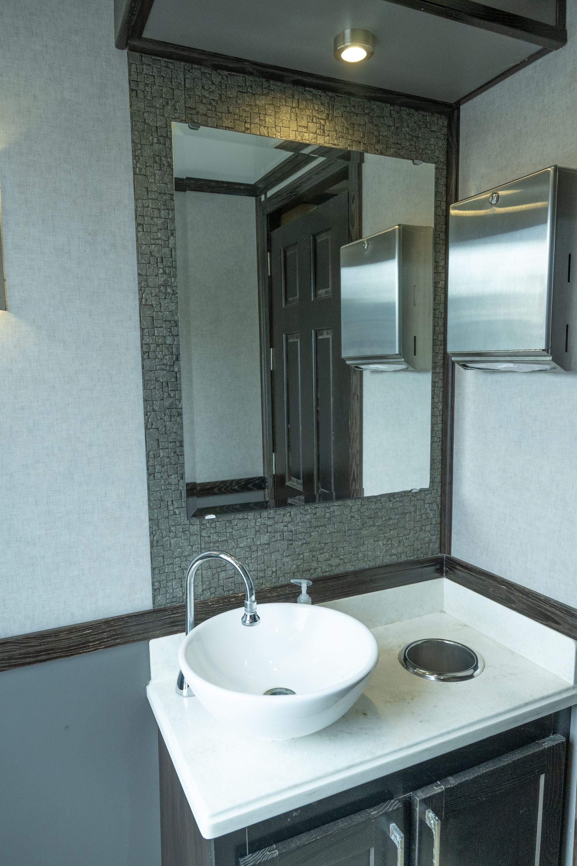 Bathroom sink with mirror, soap dispenser, paper towel dispenser. White bowl sink, wood vanity.