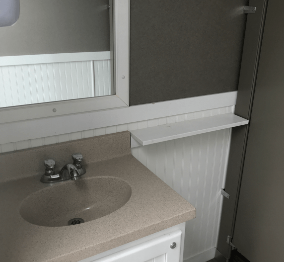 Bathroom interior: sink with faucet, mirror, shelf, white paneling, and a door.