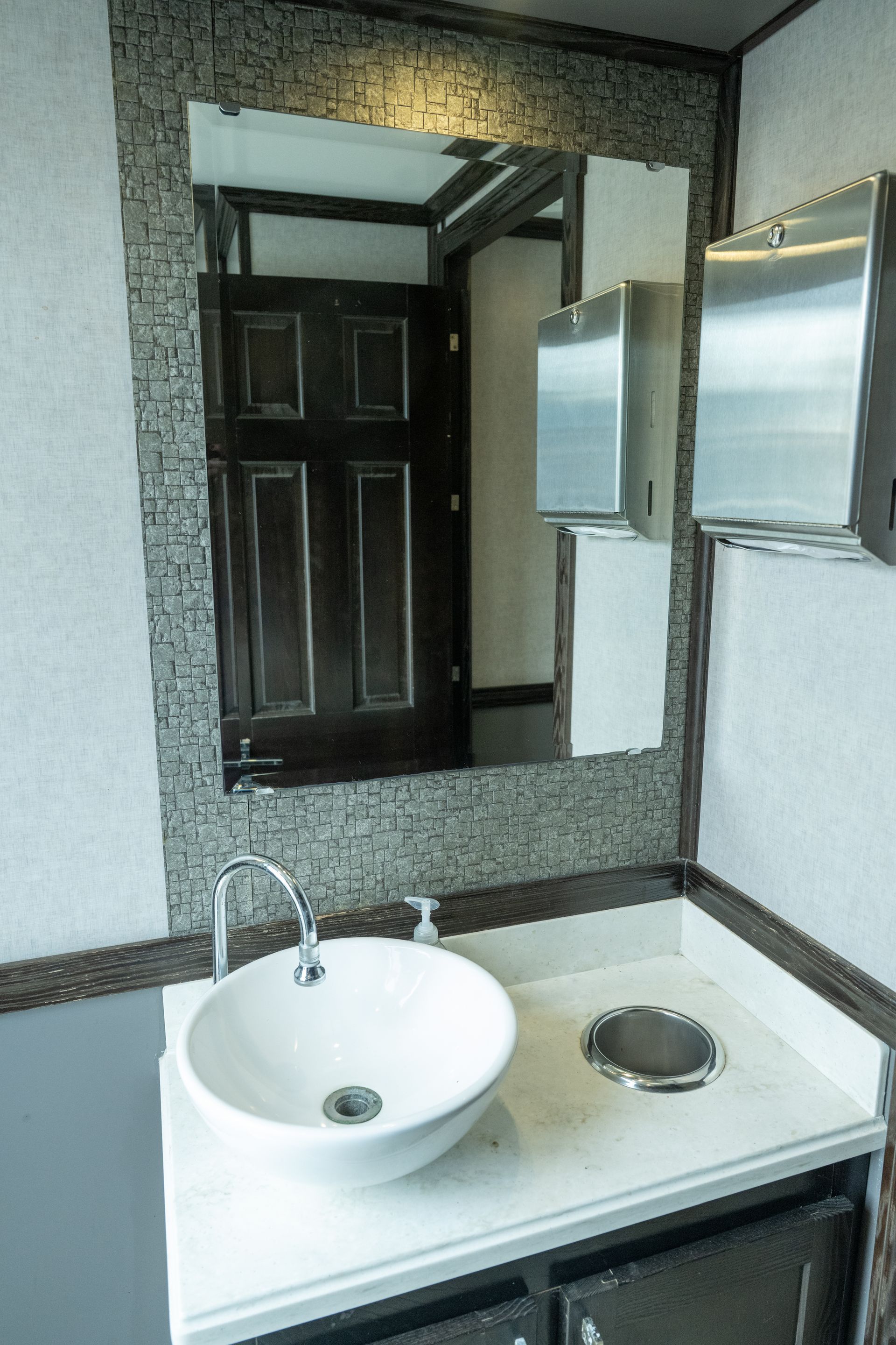 Bathroom interior with sink, mirror, and stainless steel fixtures; dark wood door visible.
