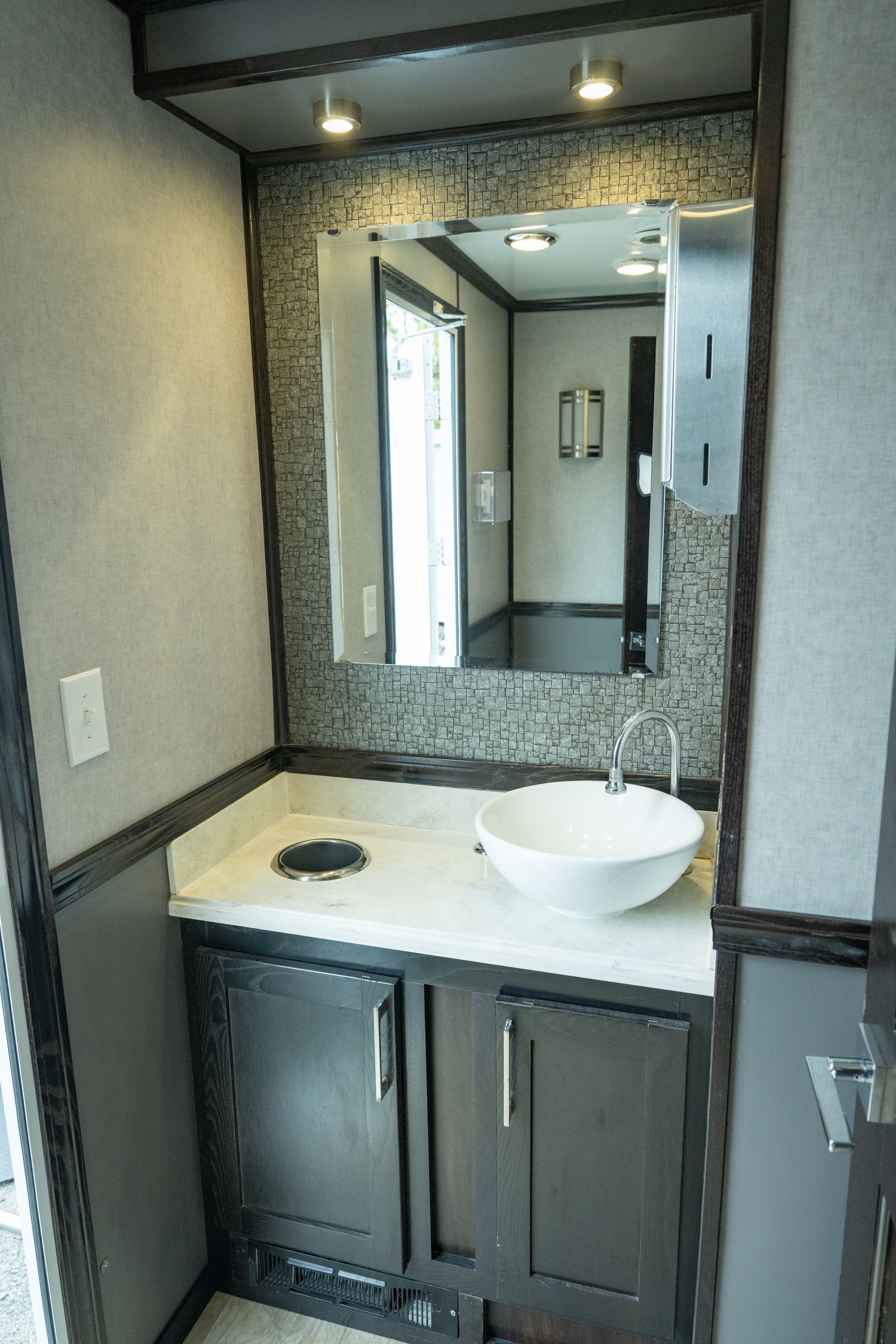 Interior of a luxury portable restroom. Sink, mirror, and cabinetry in a modern design with neutral colors.
