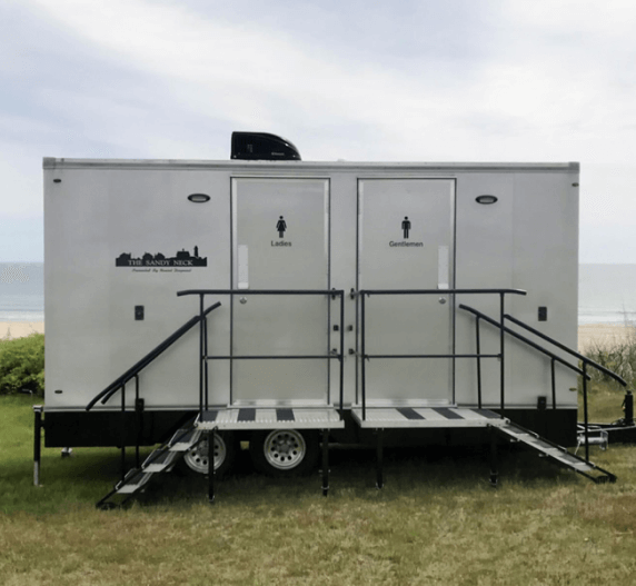 White portable restroom trailer with ramps, beach background.