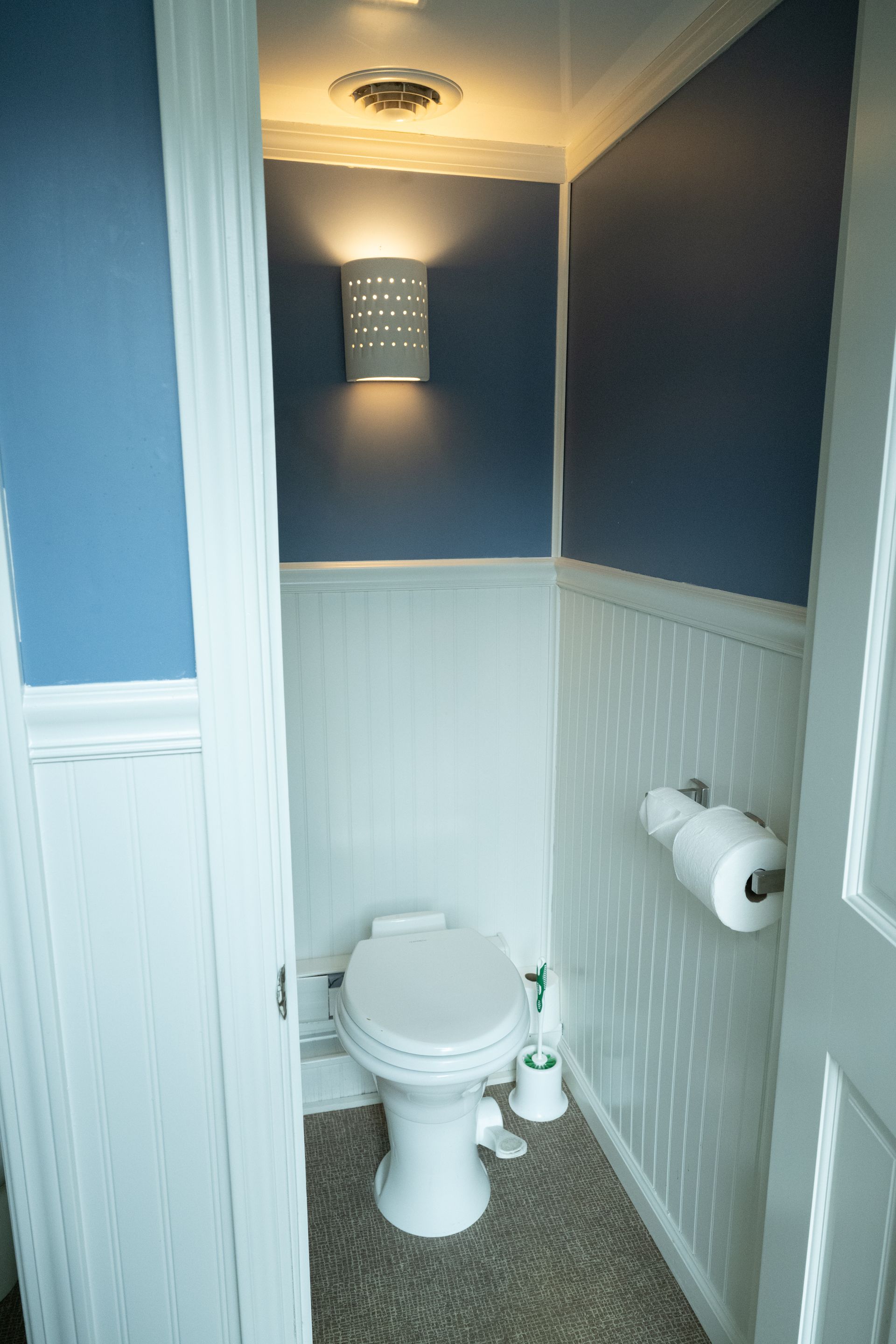 Small blue and white bathroom with a toilet and a wall-mounted light fixture.
