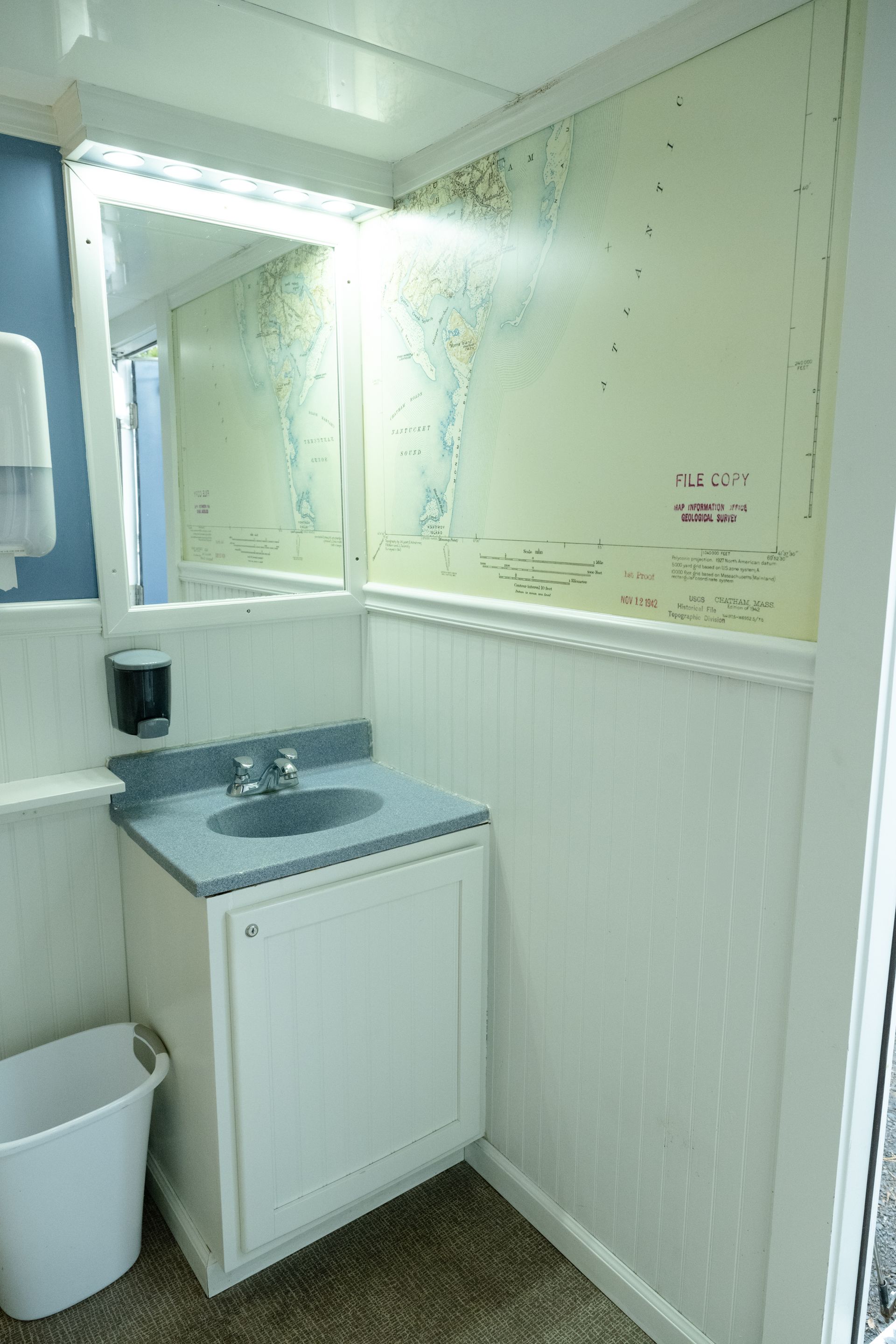 Interior of a small bathroom: white walls, sink, mirror, and trash can.