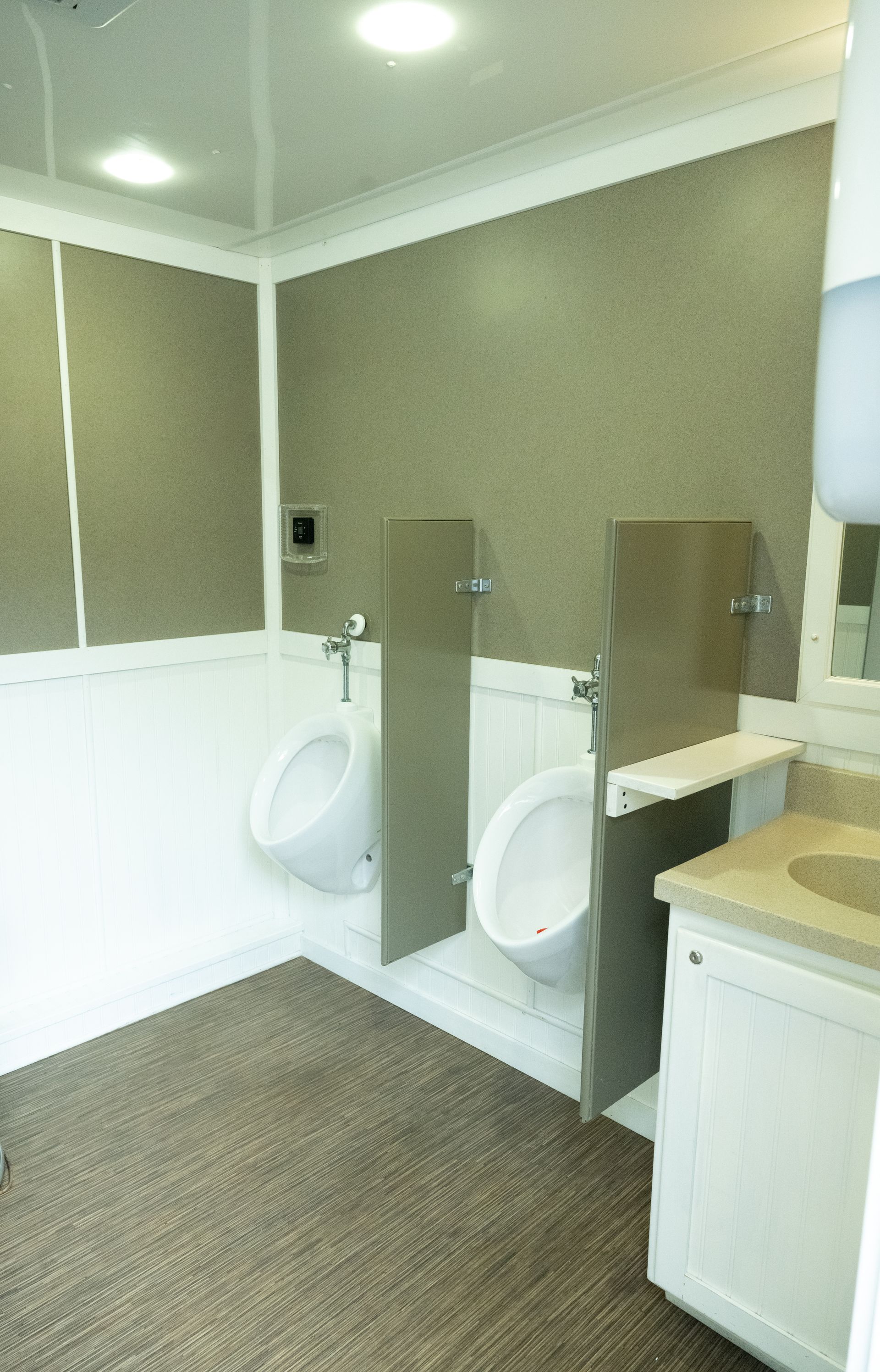 Public restroom with two urinals separated by stainless steel dividers. White and brown color scheme.
