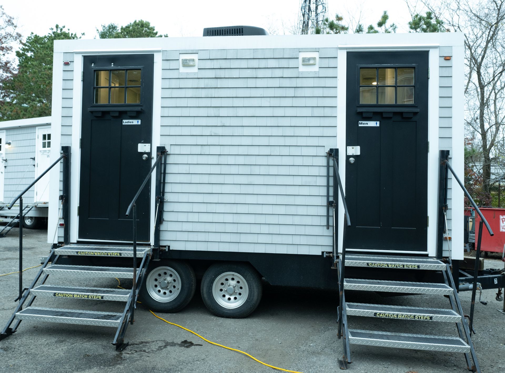 Gray portable restroom trailer with two black doors, stairs, and handrails.