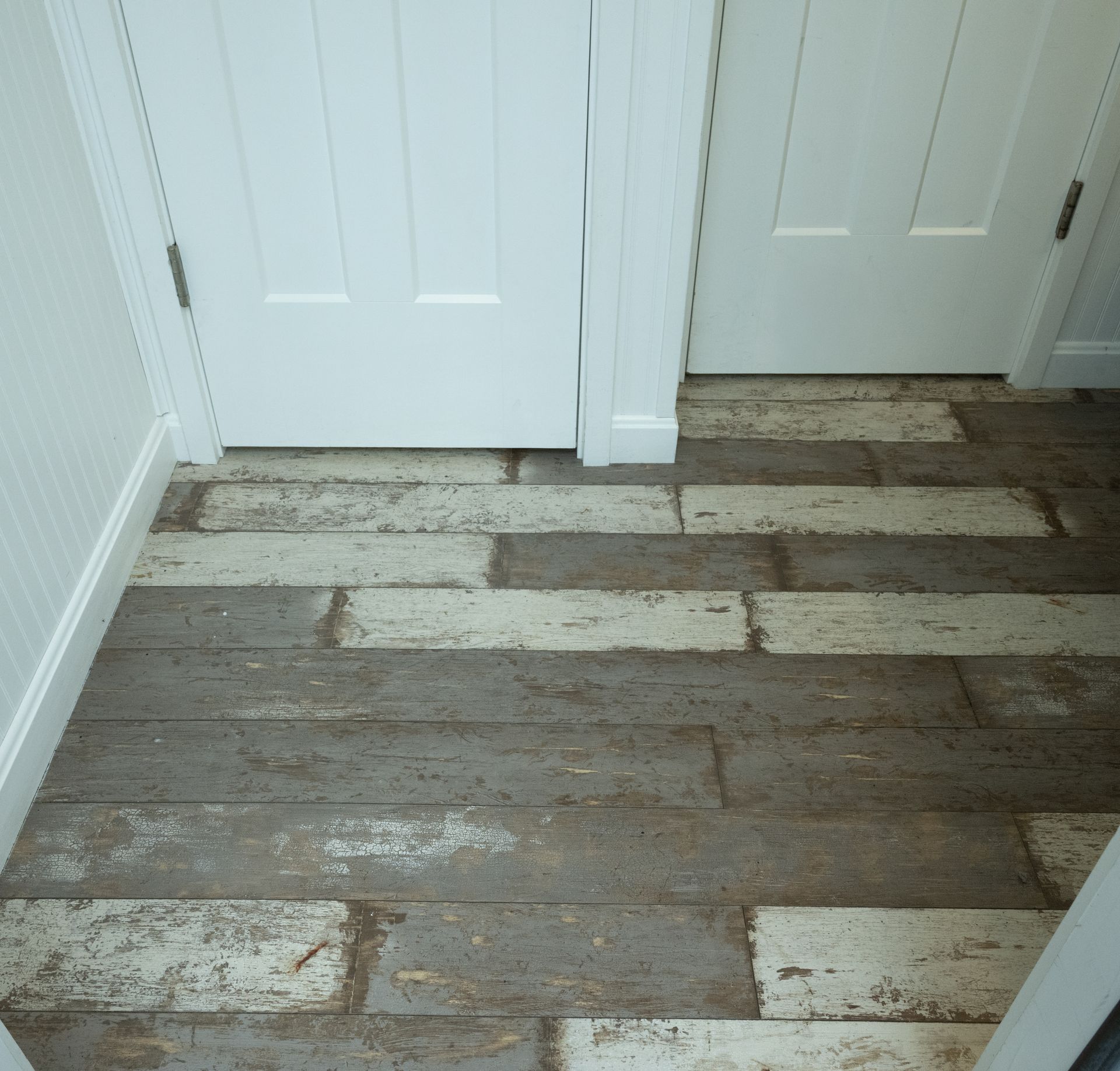 View of a room's rustic floorboards in shades of grey and white, near two white doors.