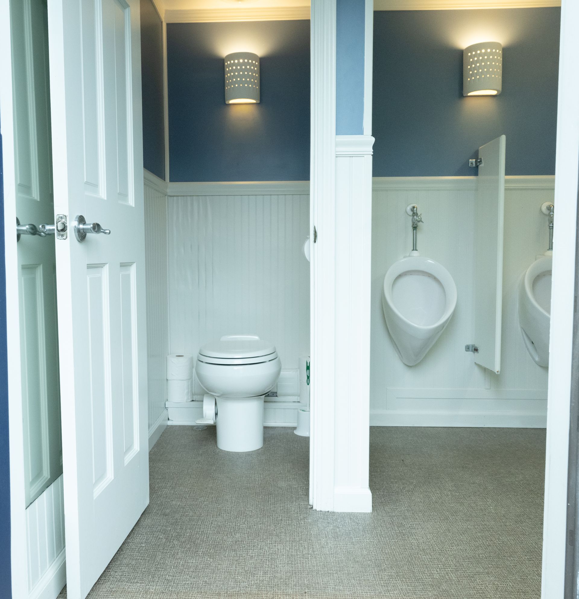 Public restroom with a toilet, urinals, and white doors and paneling, and blue walls.
