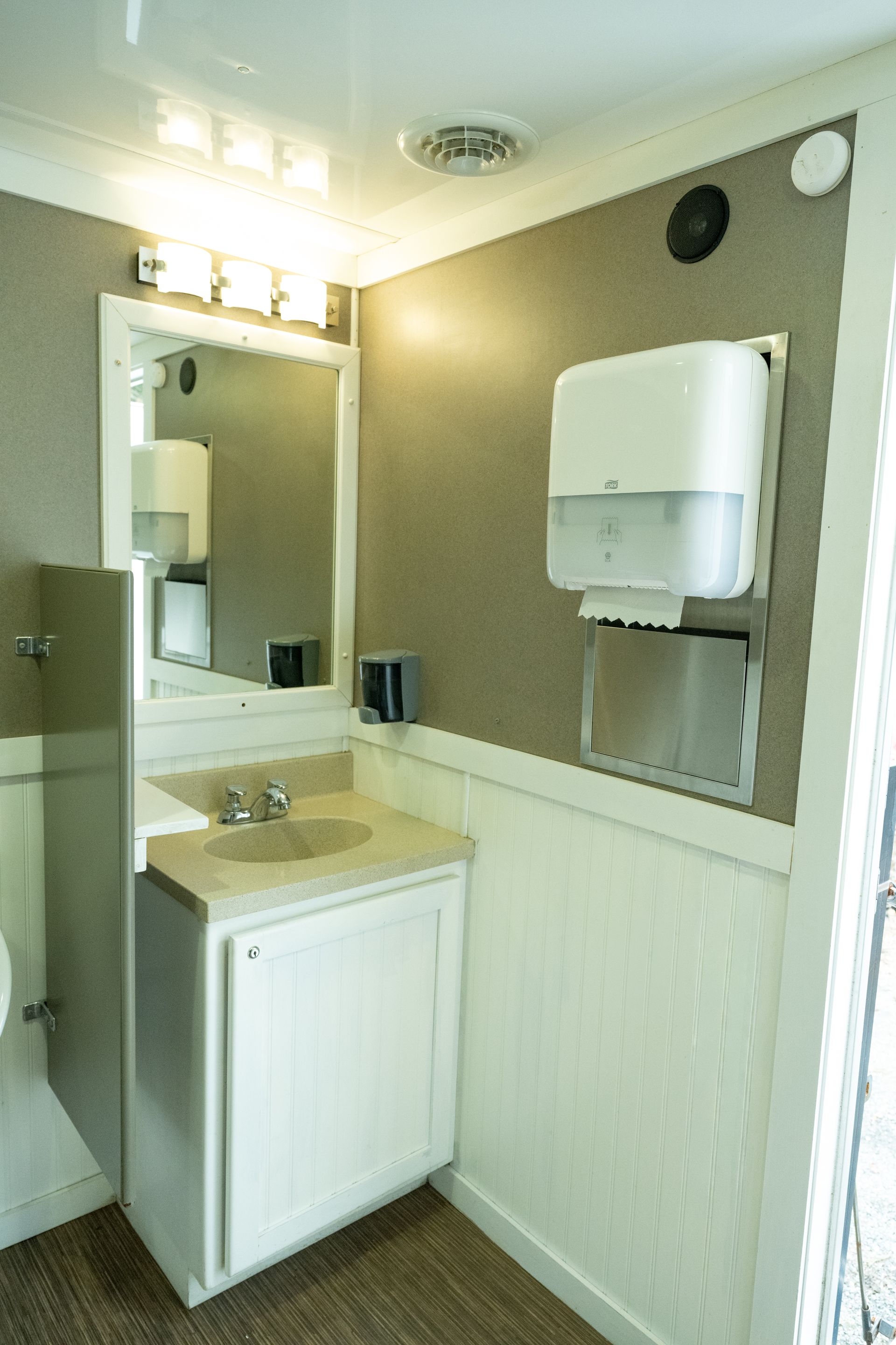 Interior of a restroom with sink, mirror, paper towel dispenser, and textured walls.