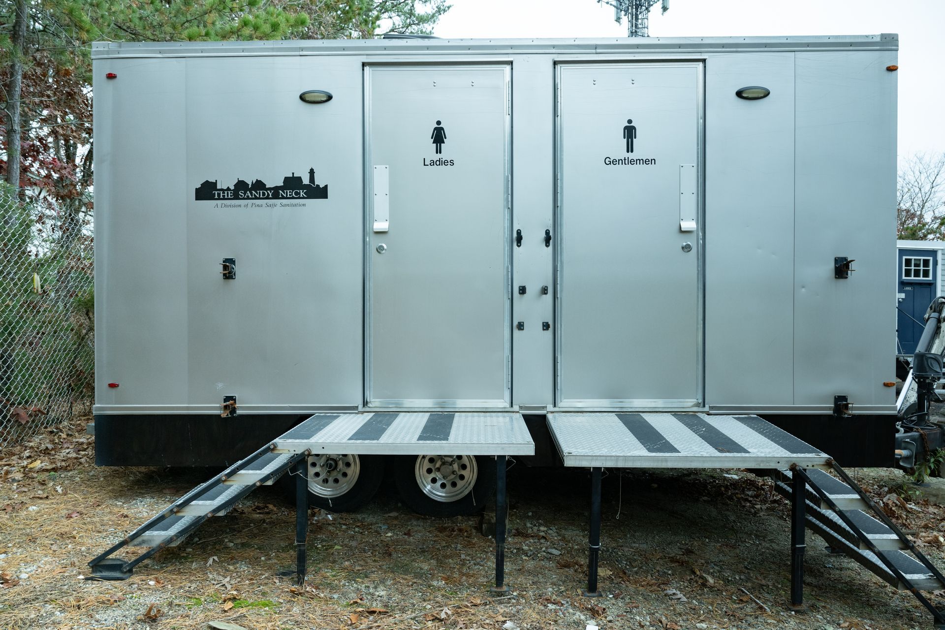 Silver portable restroom with separate entrances for women and men, each with ramp access.