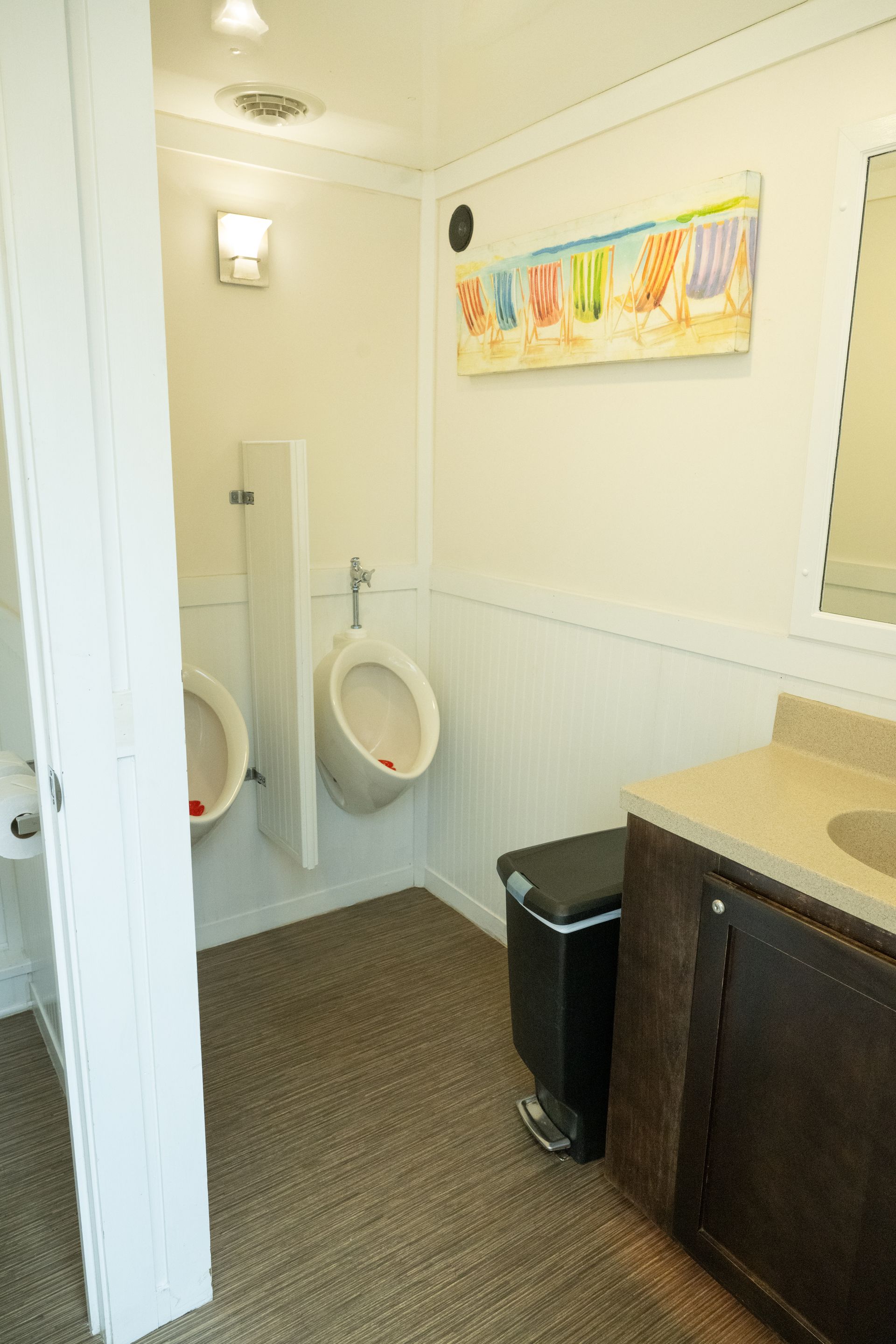 Interior of a clean portable restroom with urinals, a sink, and a trash can.