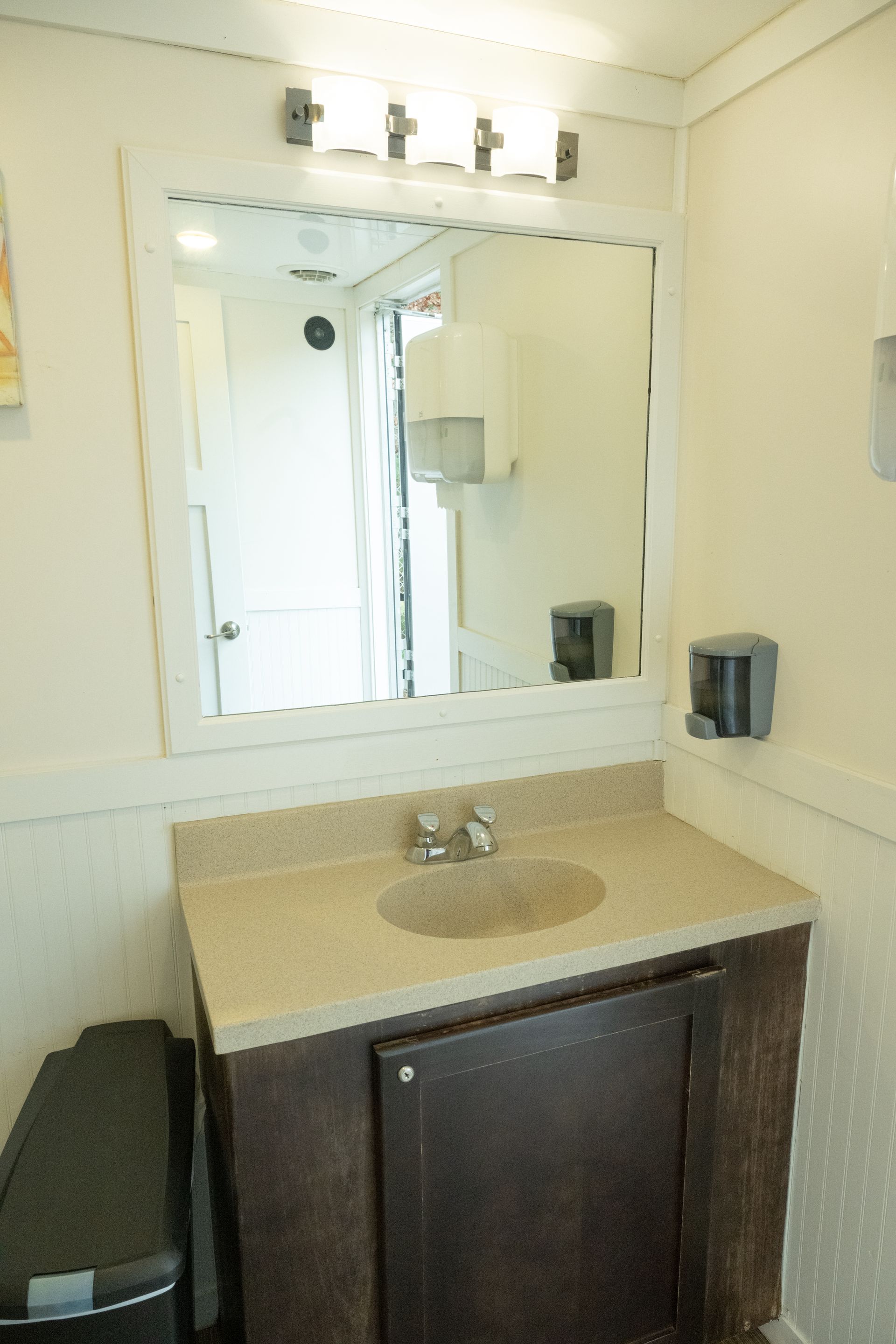 Bathroom with a sink, mirror, and cabinet. The room is brightly lit, likely a portable unit.