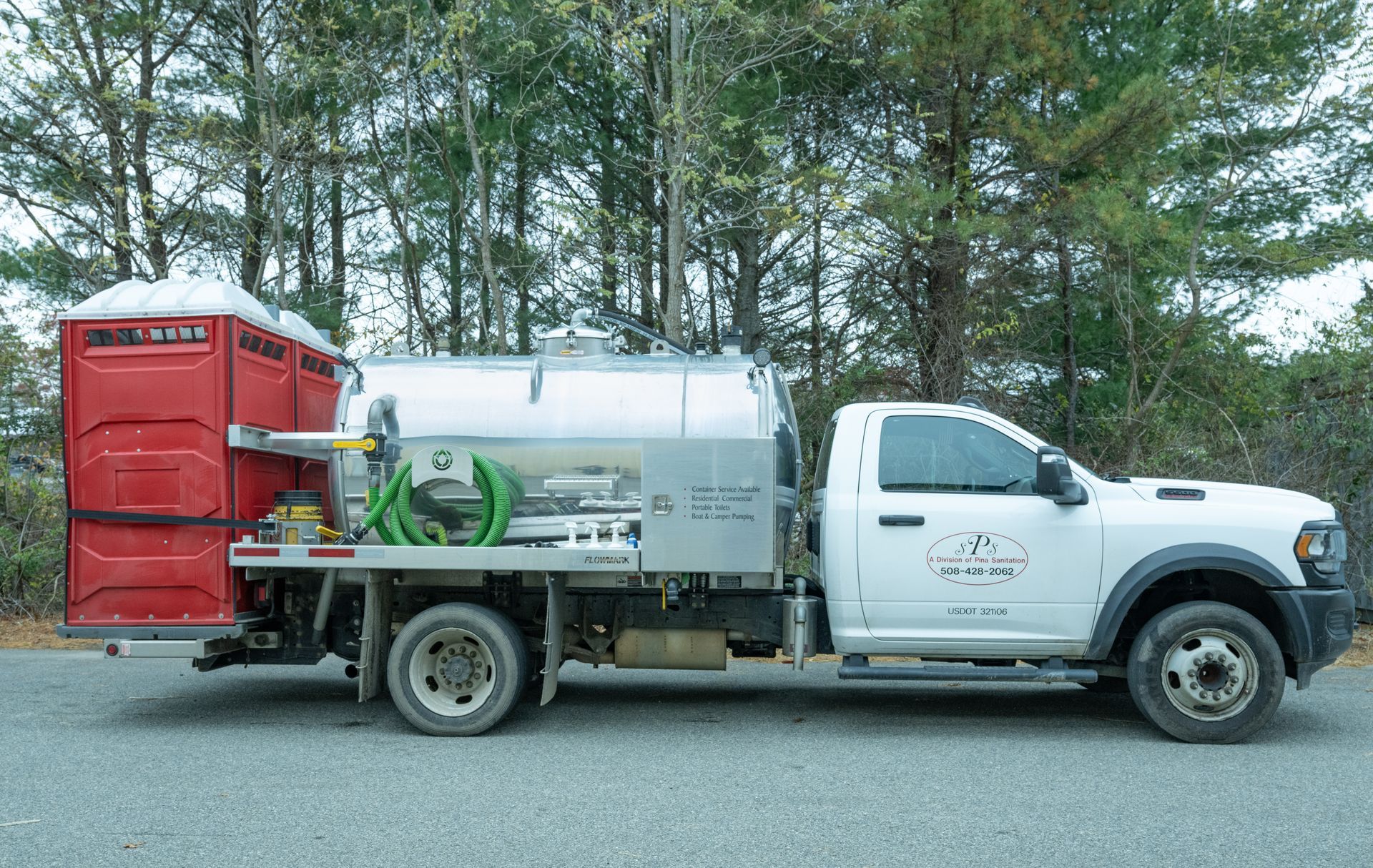 White truck with portable toilets, parked on the side of a road, with trees in the background.