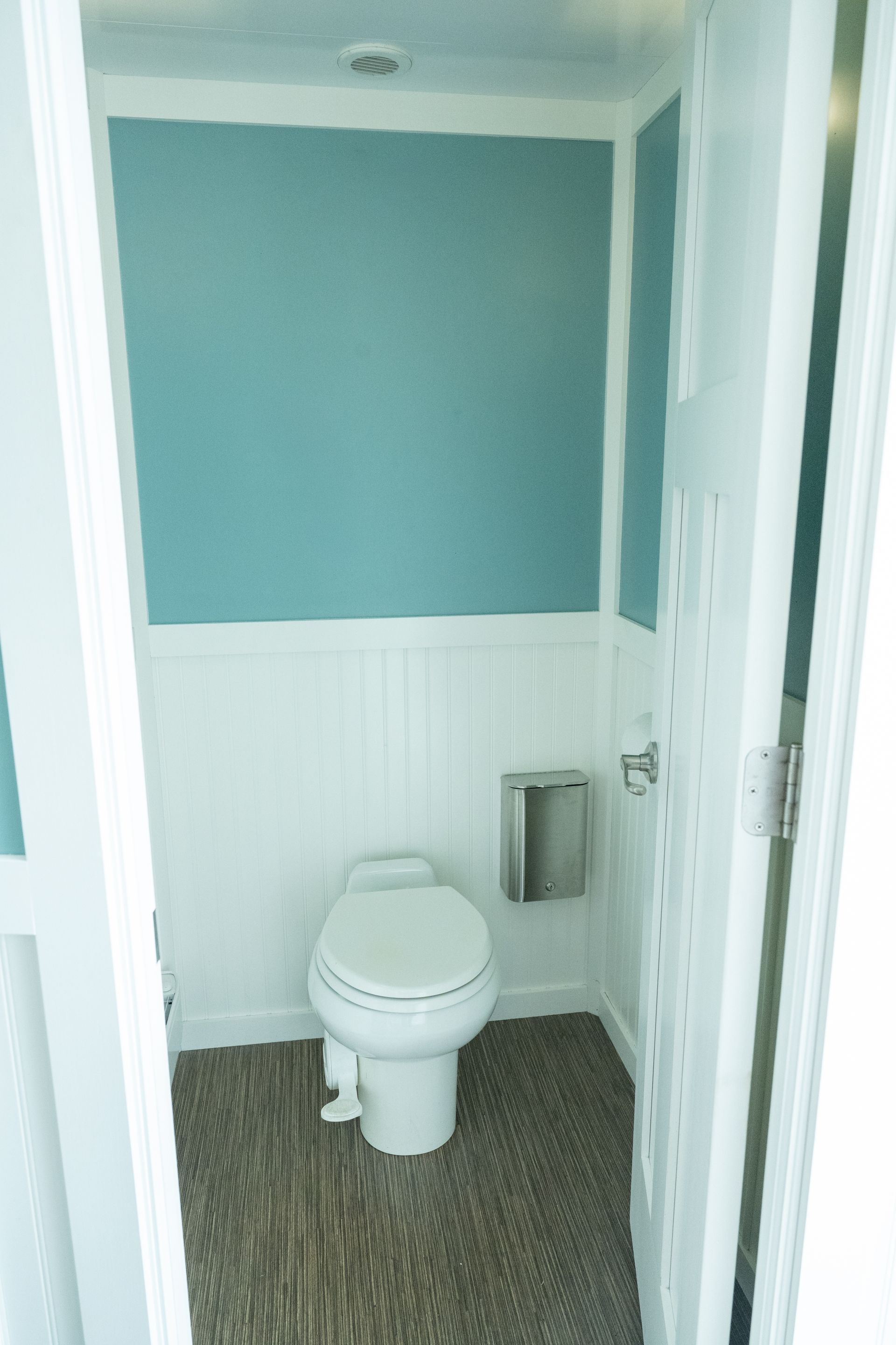 Small bathroom with white walls, teal upper wall, toilet, and a pebble-like floor.