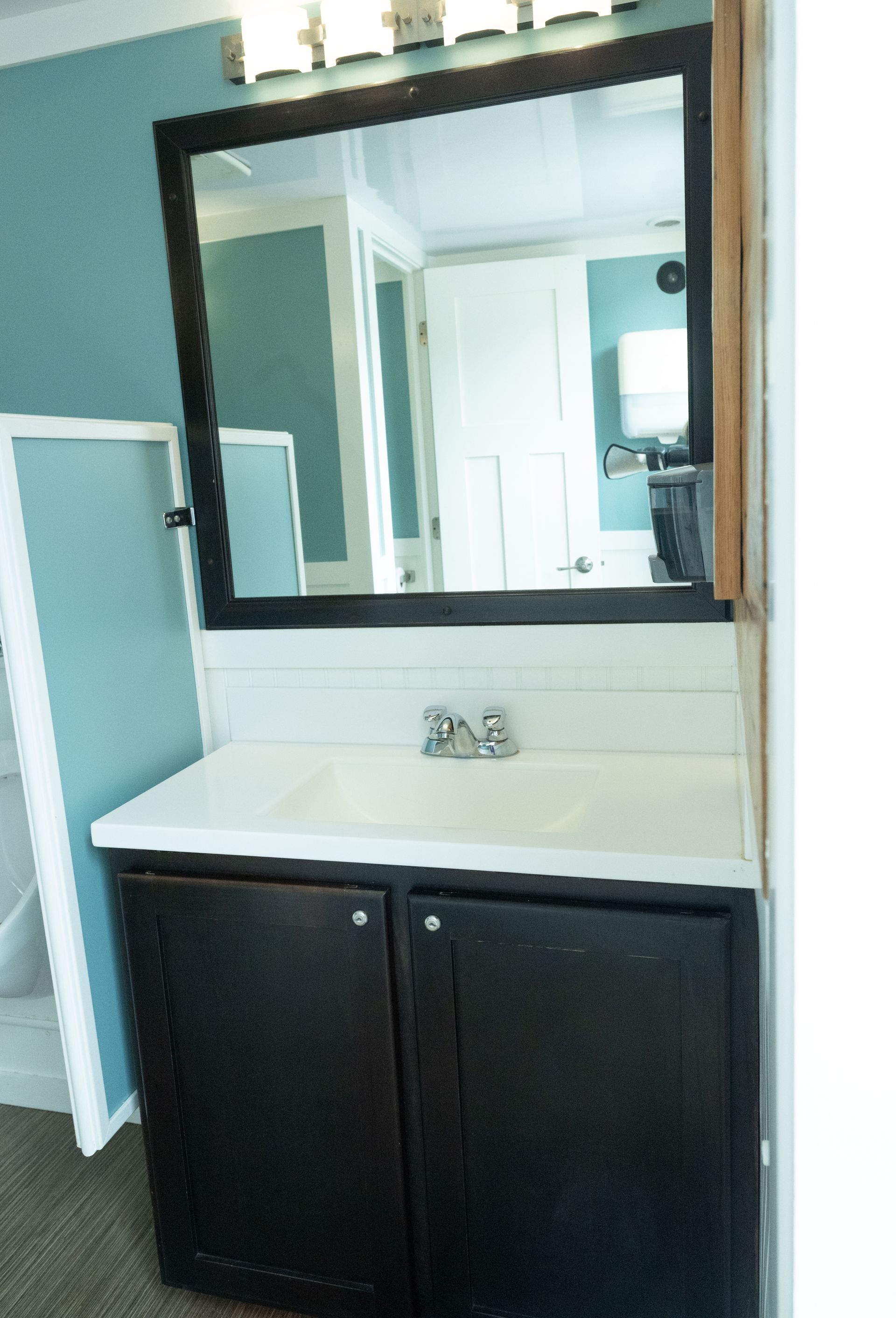 Bathroom vanity with black cabinet, white countertop, and large mirror. Blue wall.