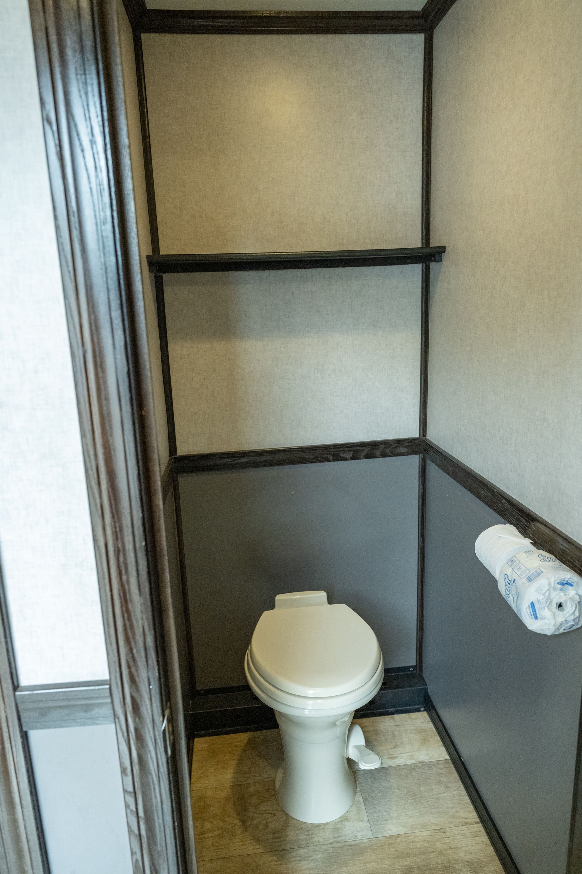 Small RV bathroom with toilet, shelves, and toilet paper. Walls are beige and gray.