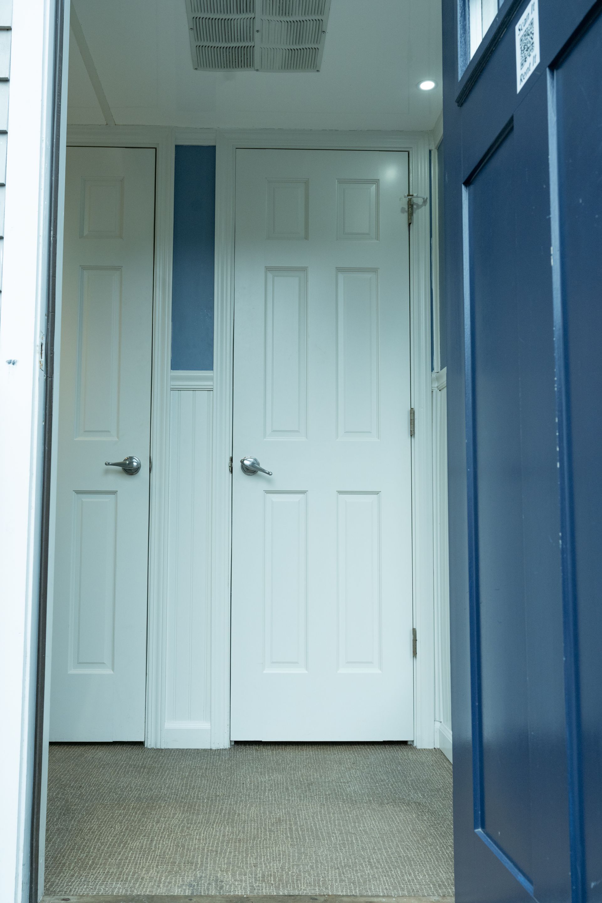 Blue door slightly ajar revealing two white doors and a narrow blue panel in a hallway with carpet.