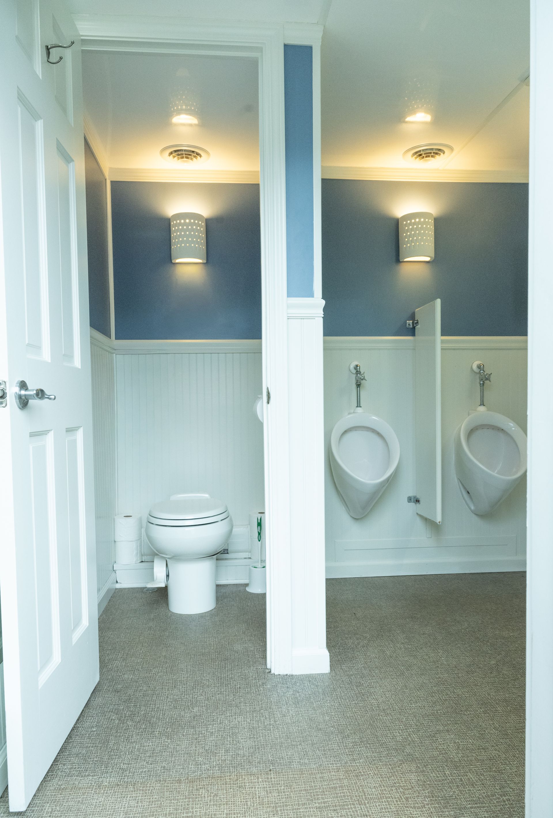 Public restroom with two urinals and a toilet, blue walls, white trim, and a gray speckled floor.