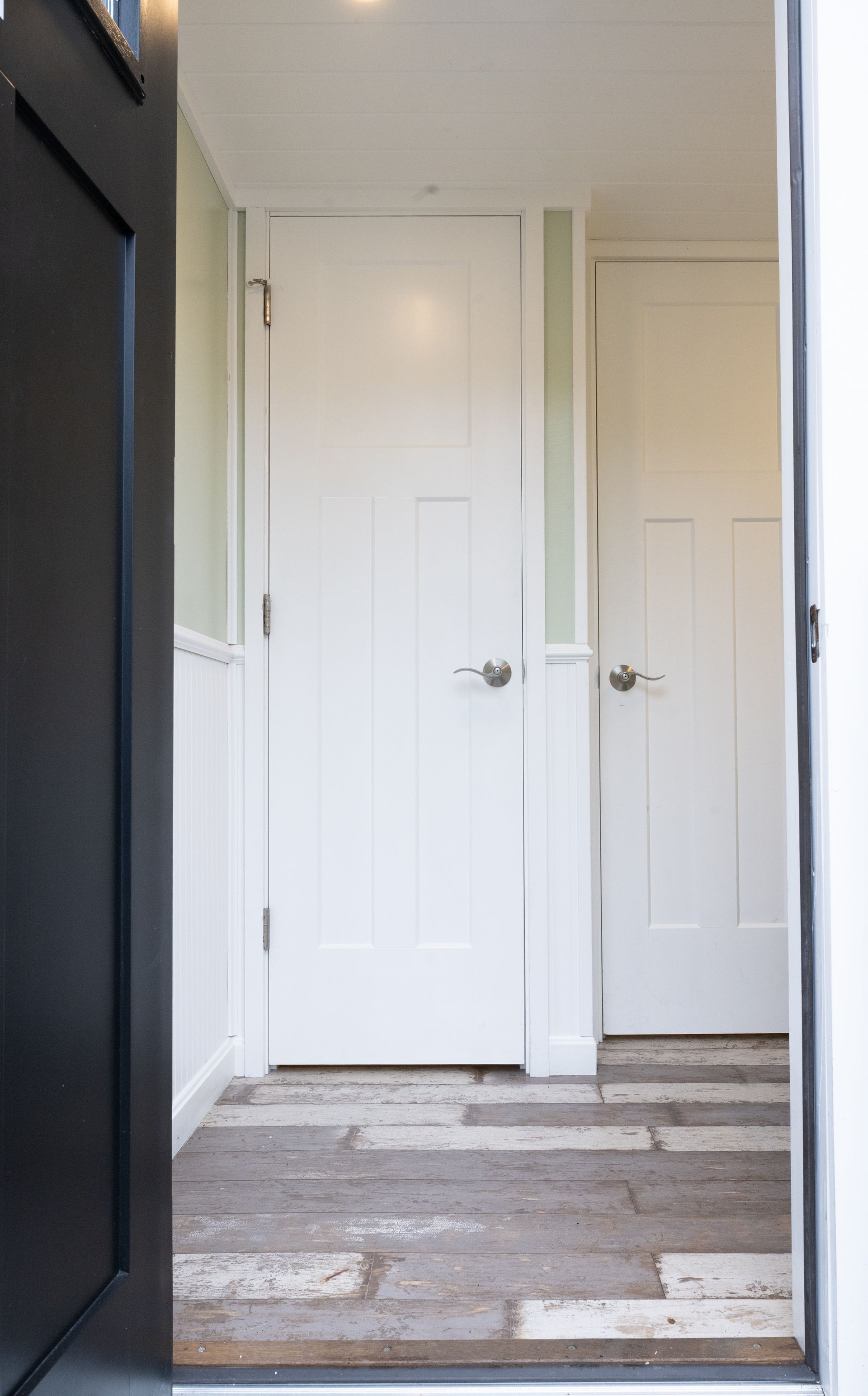 View from a doorway into a hallway with two white doors, a black doorframe, and light wood flooring.