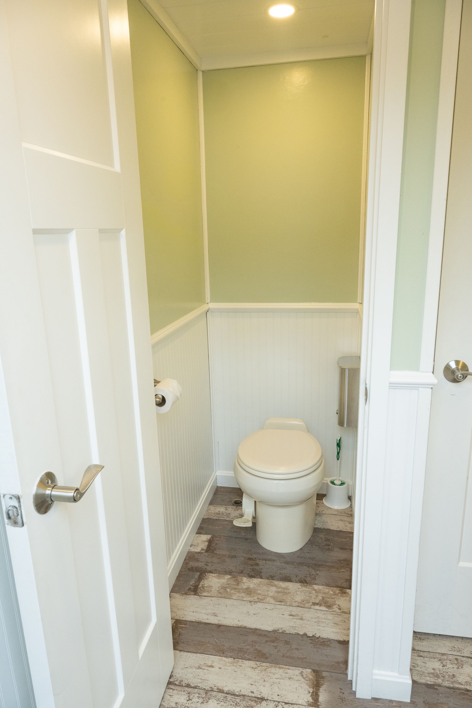 Small bathroom with toilet and door, white and green walls, patterned flooring.