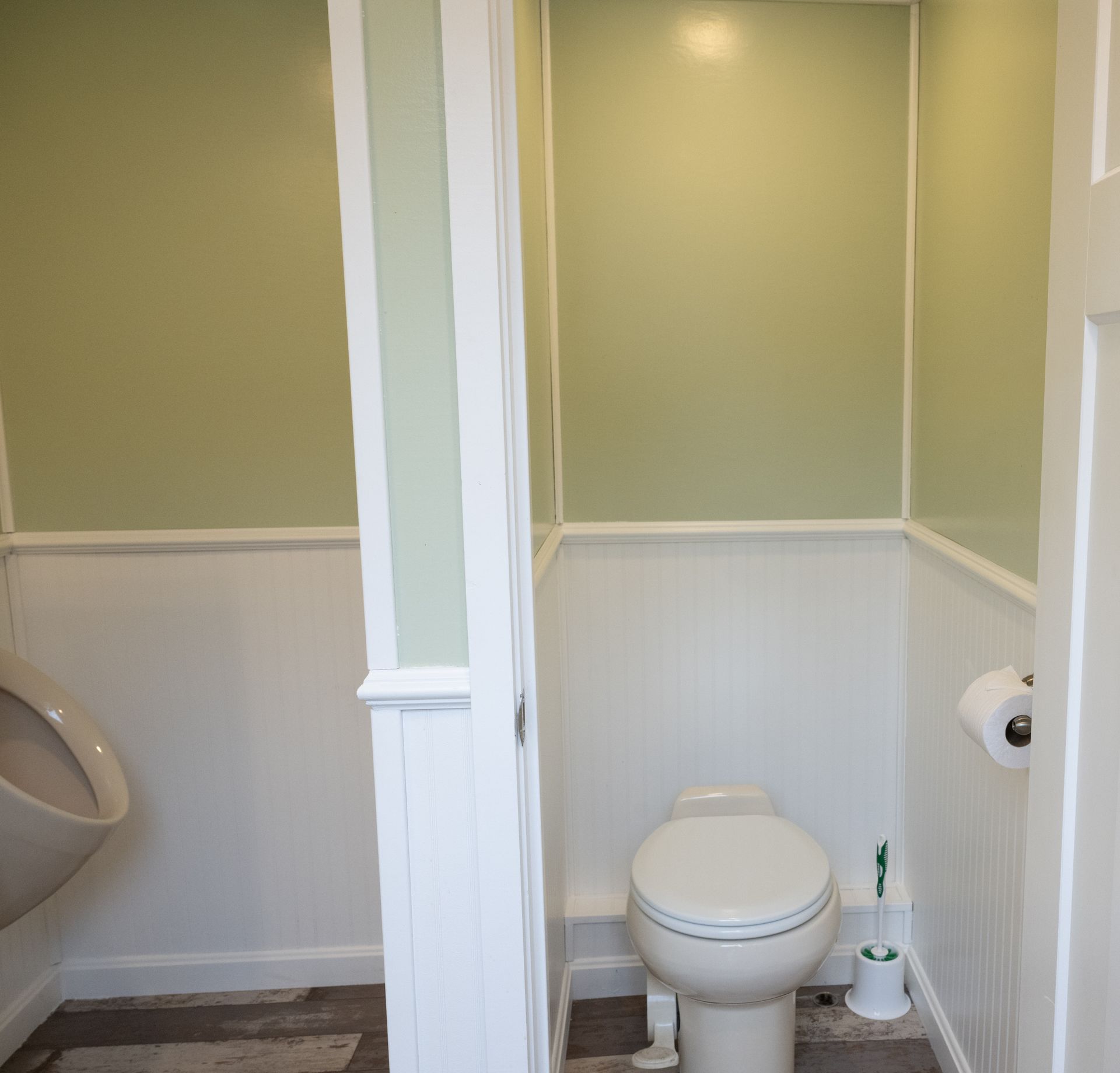 Public restroom with a urinal and toilet, white and green walls, and beadboard paneling.
