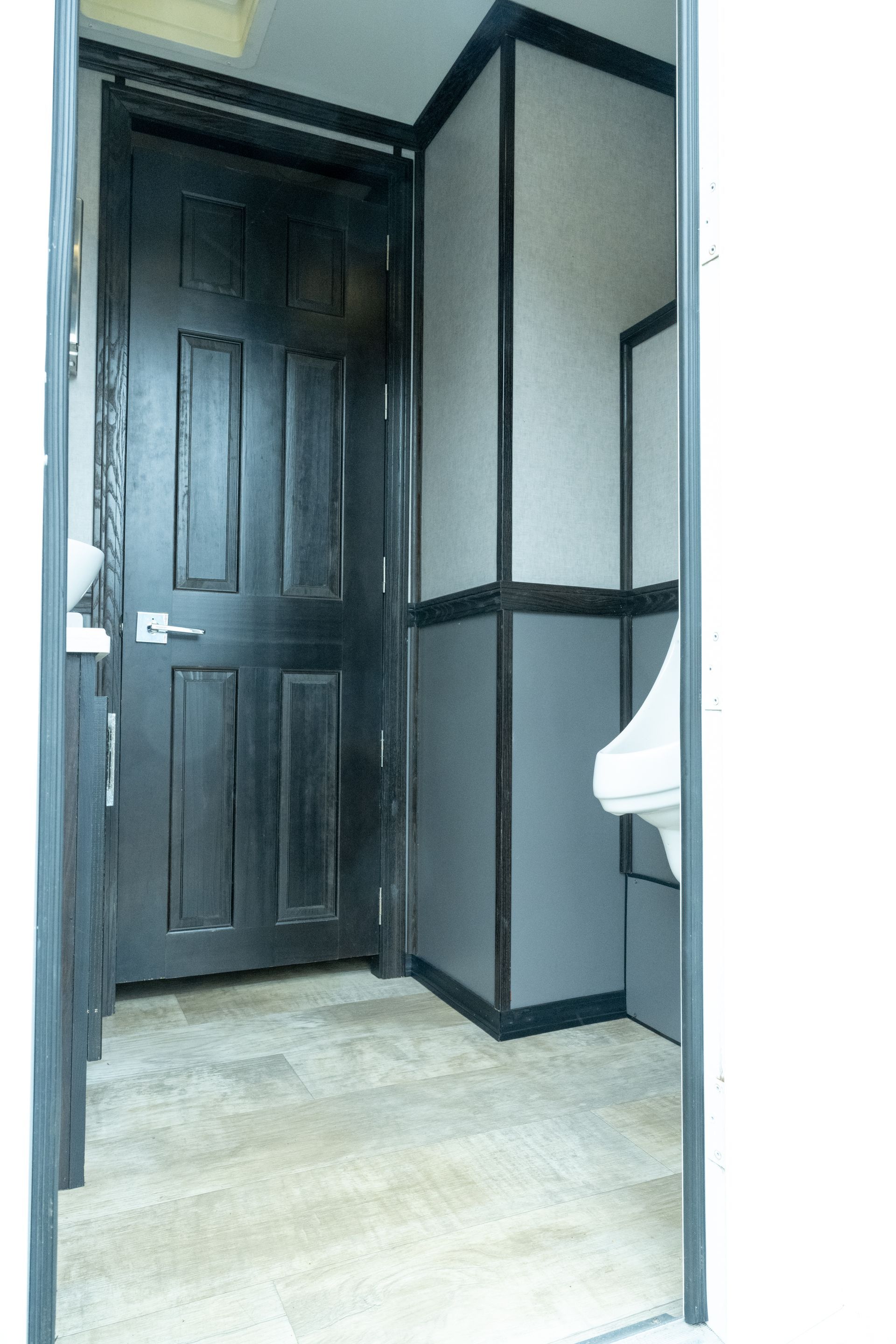 Interior of a dark-paneled restroom with a door, urinal, and gray and white walls.