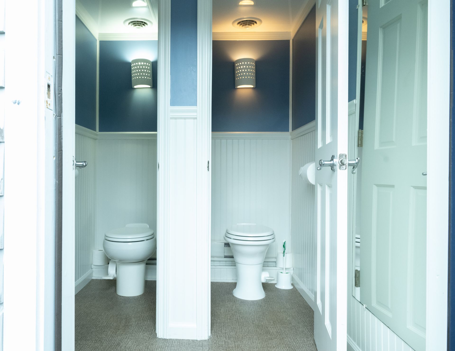 Two adjacent public bathroom stalls with blue walls, white trim, and doors.