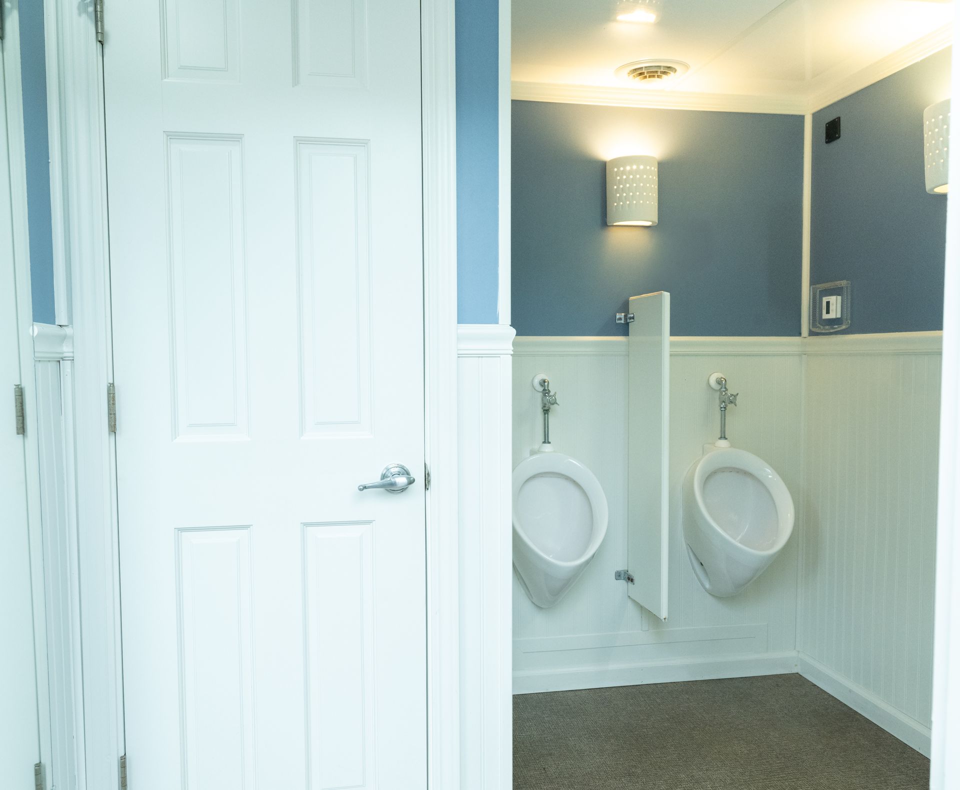 Public restroom with two urinals, blue wall, white trim, and a closed white door.