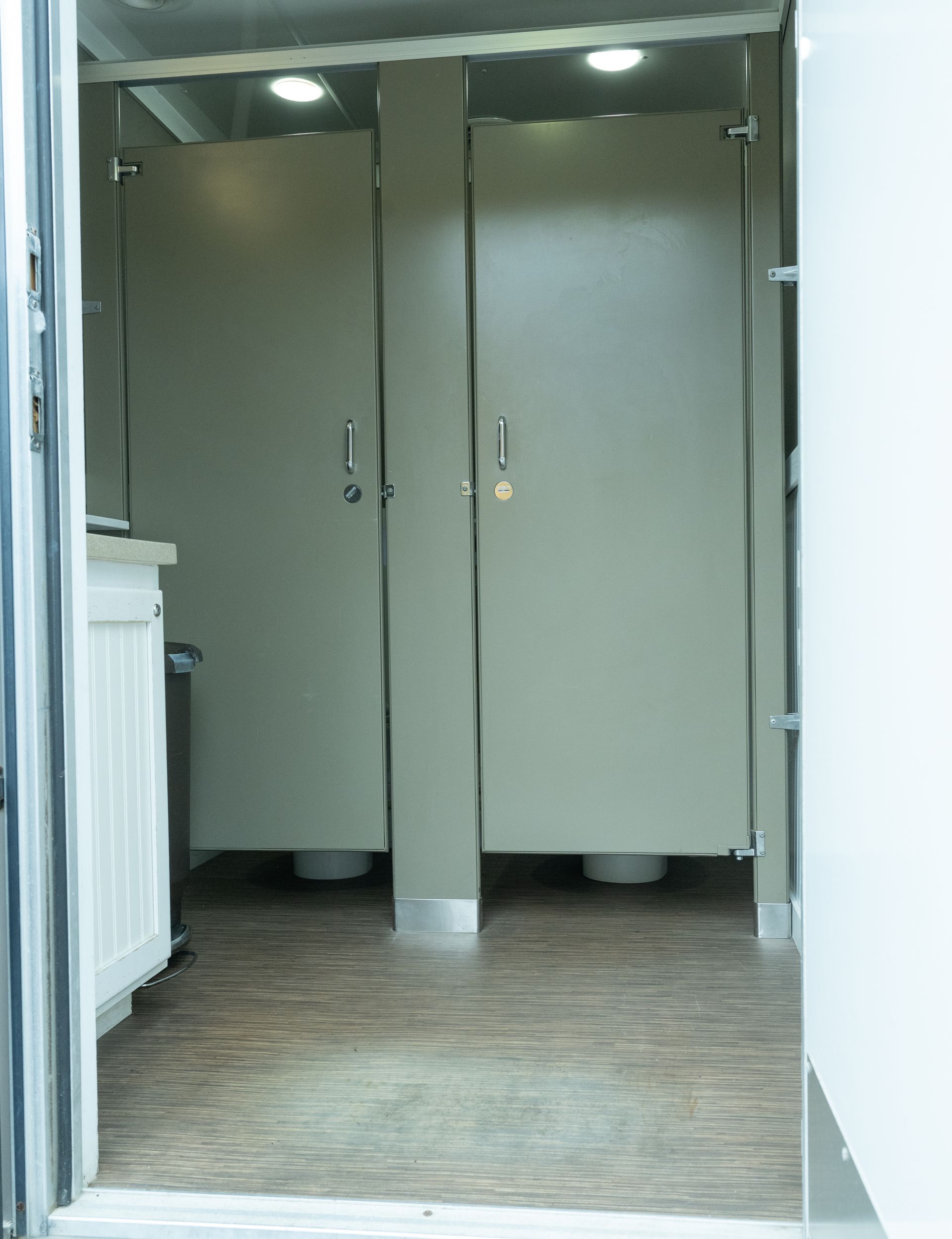 Interior of a restroom trailer with two stalls and a sink.