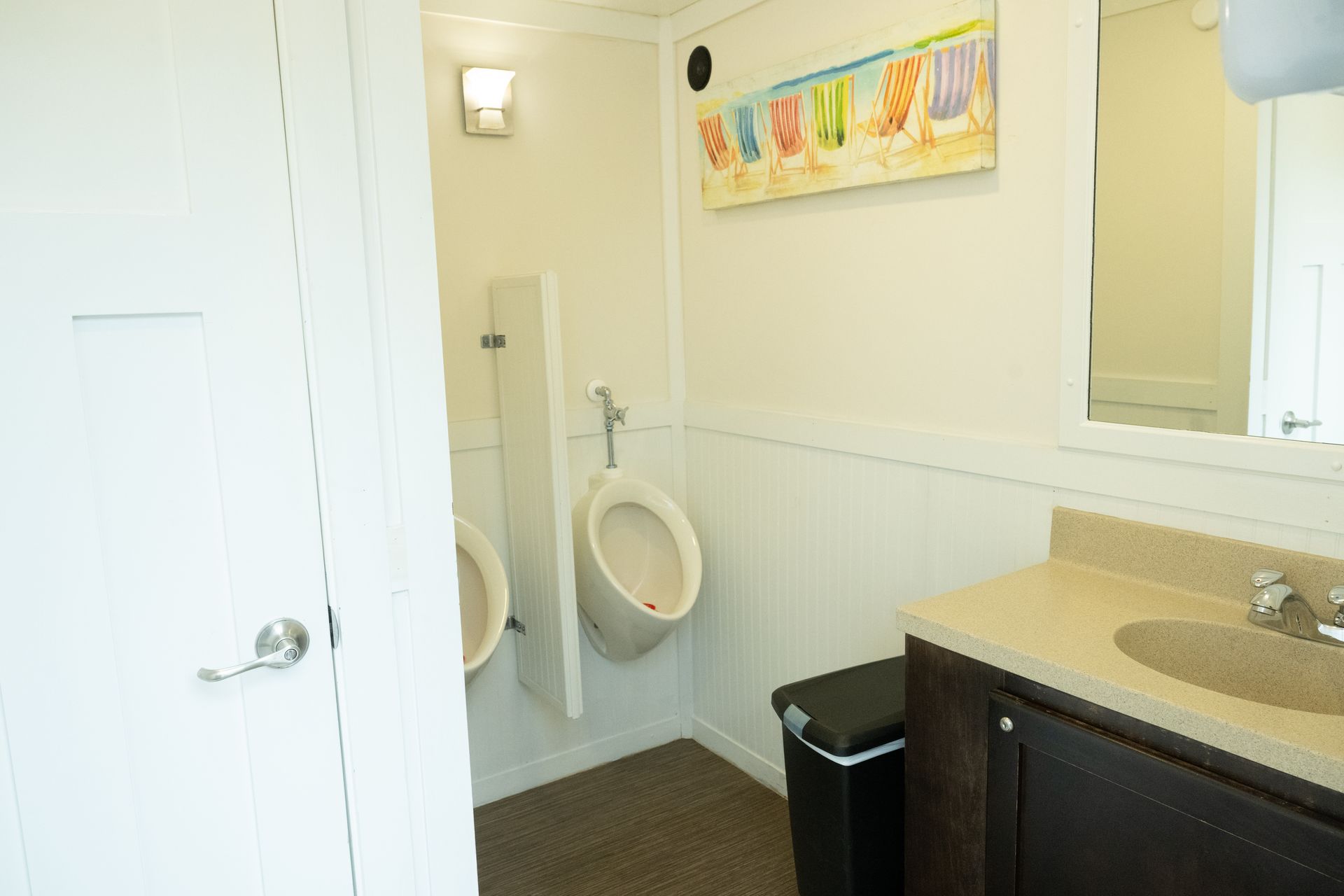 Bathroom with two urinals, a sink, and a framed beach scene.