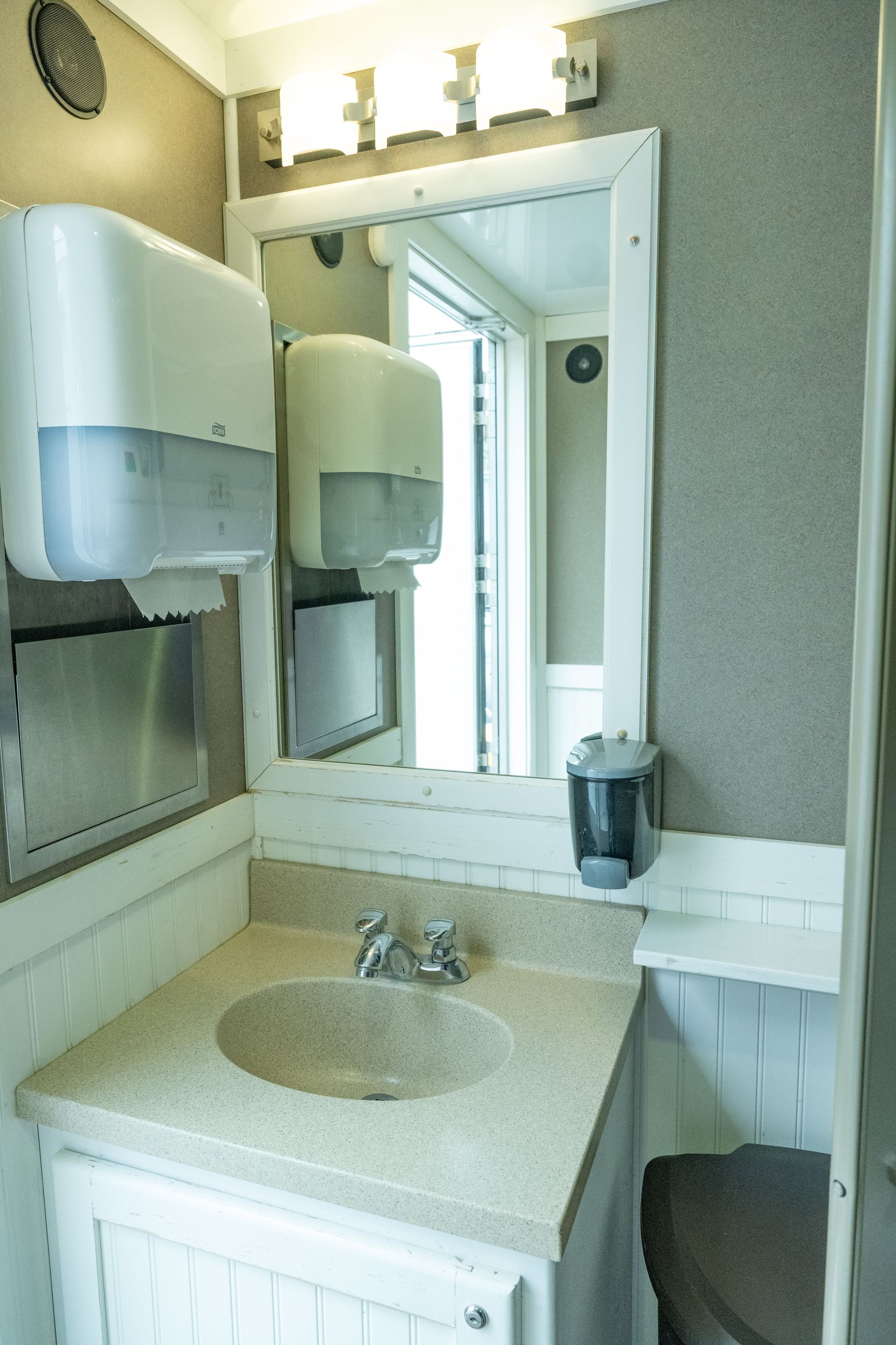 Bathroom interior with sink, mirror, soap dispenser, and paper towel dispensers. White and beige tones.