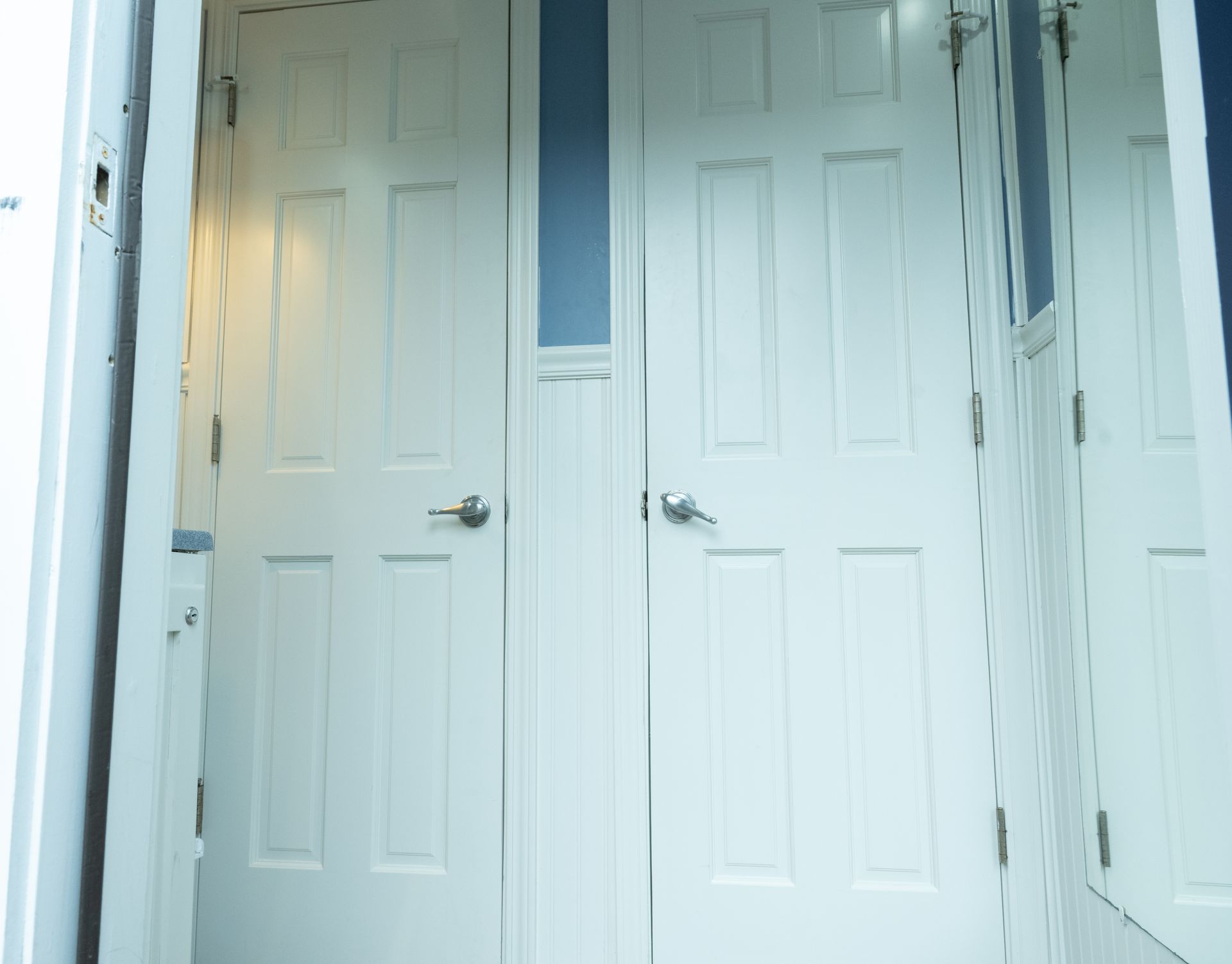 White doors, two side-by-side, with a small blue window between them, reflecting a room.