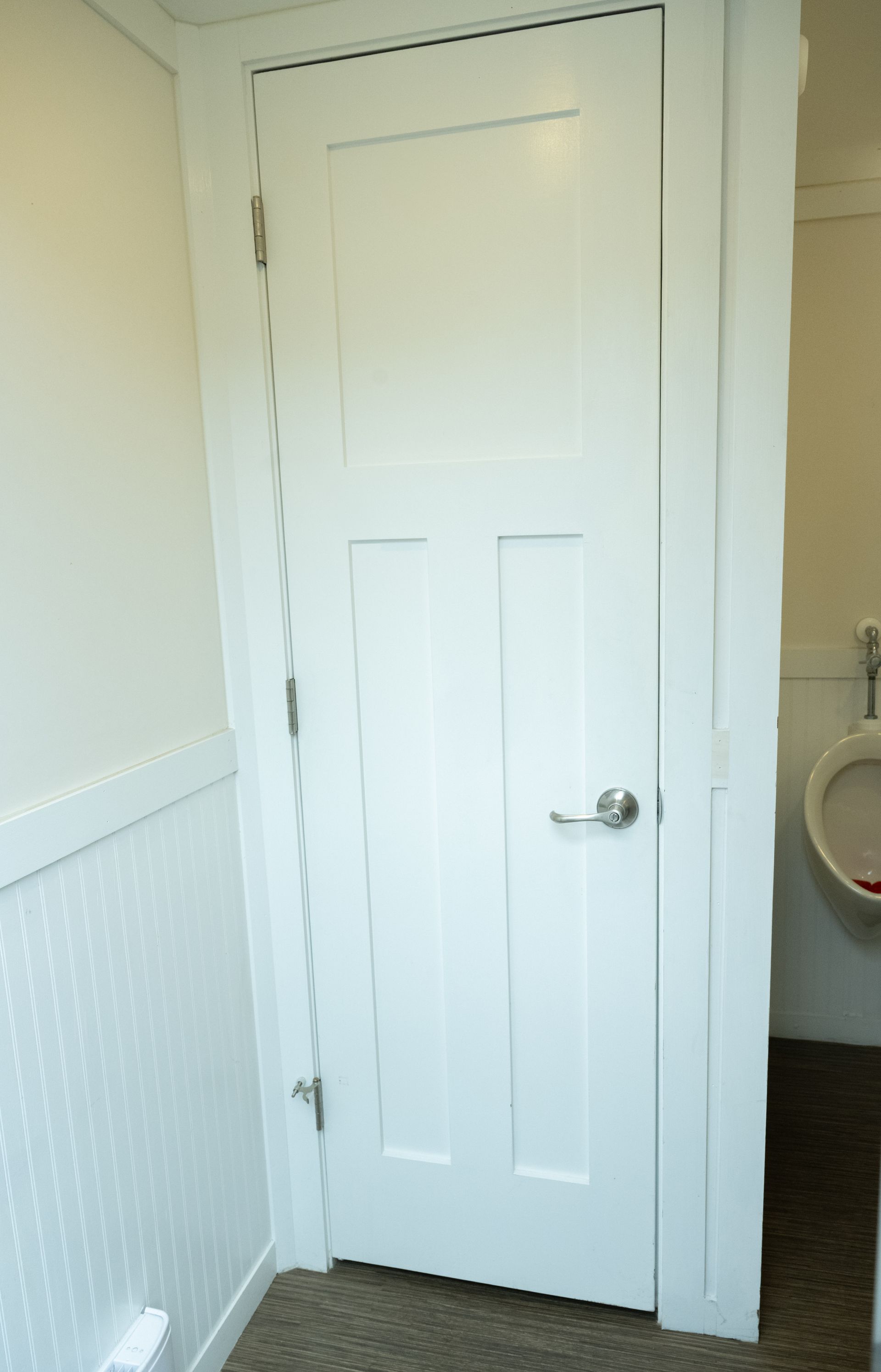 White interior door in a restroom, with a doorknob, next to a white wall.