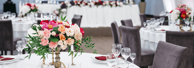 A banquet hall set for a wedding reception with floral centerpieces on round tables and white tablecloths.