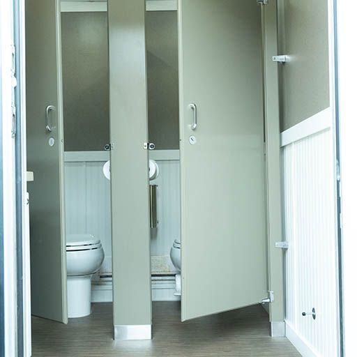 Open restroom stalls with gray doors and white toilets in a tiled bathroom