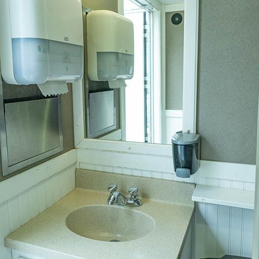 Public restroom sink with mirror, soap dispensers, and a countertop trash bin