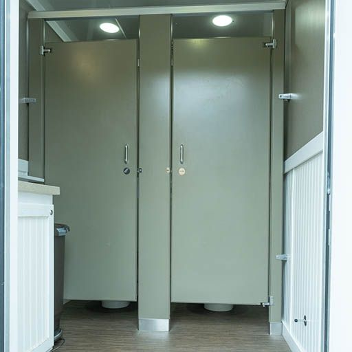 Two gray restroom stall doors in a tiled bathroom with white walls and partitions