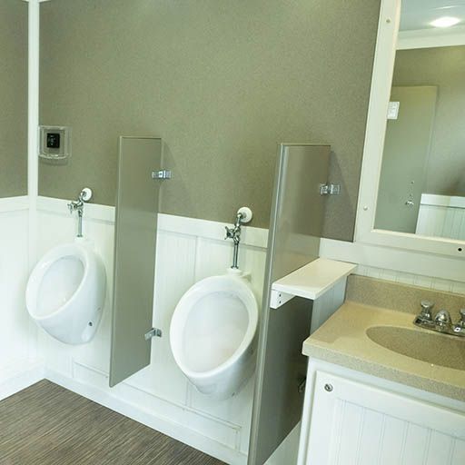 Public restroom with two urinals, privacy dividers, and a sink counter under mirrors