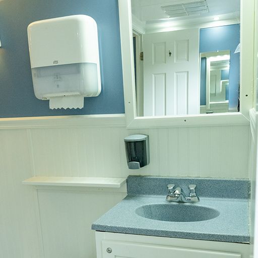 Public restroom vanity with a sink, soap dispenser, mirror, and blue-gray walls
