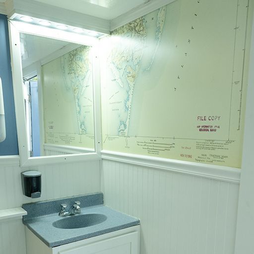 Small restroom sink with mirror, gray counter, and wall map panel in the background.