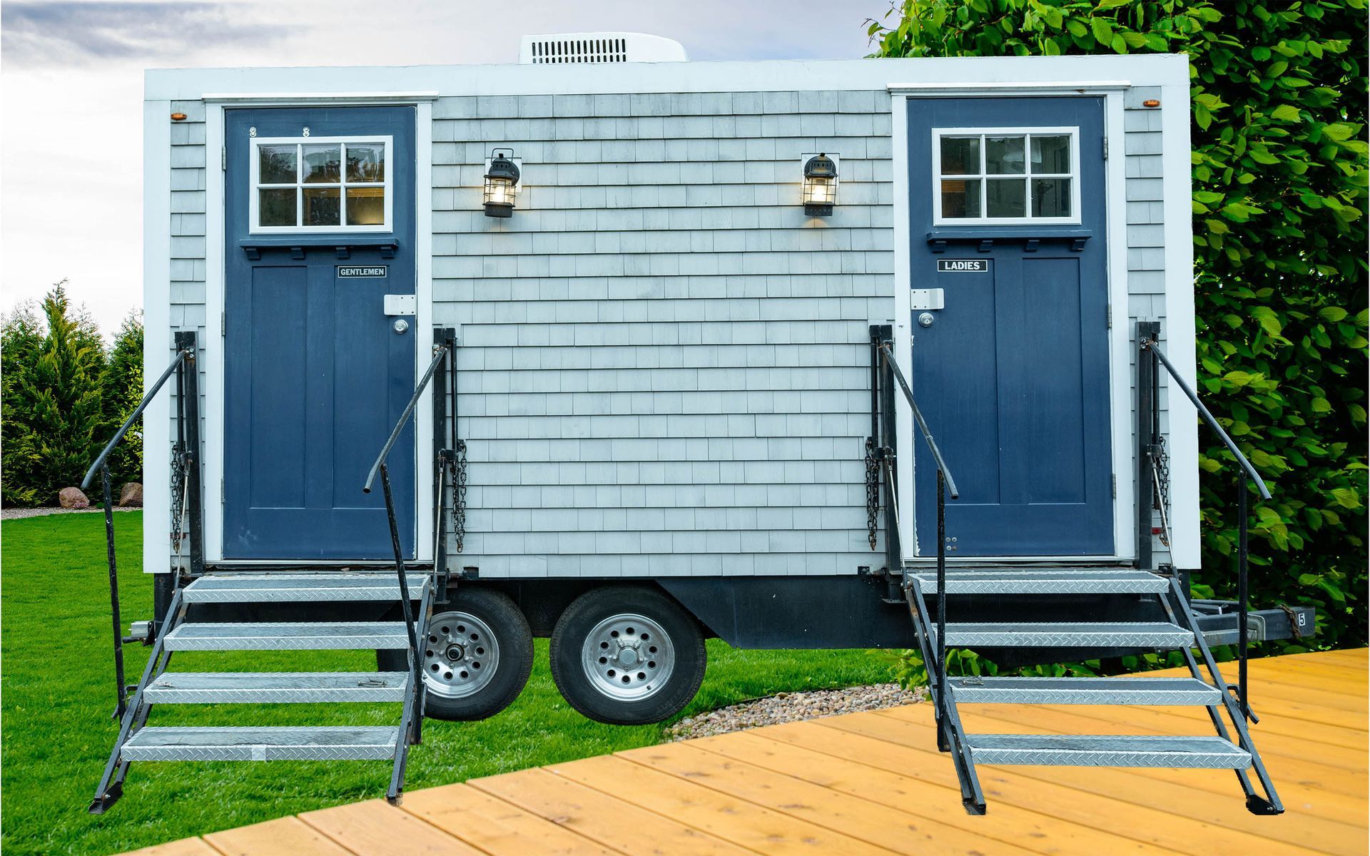 Blue tiny house trailer with two front doors and metal steps on a grassy lawn