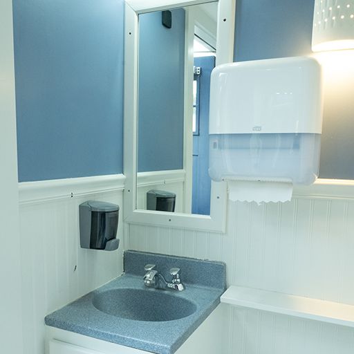 Small blue-and-white restroom with sink, mirror, soap dispenser, and paper towel dispenser