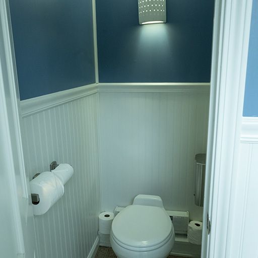 Small restroom with a toilet, white wainscoting, blue walls, and a wall light.