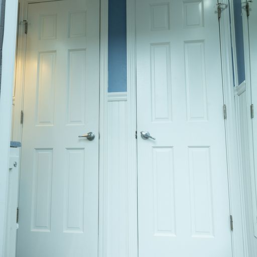 Two white closet doors with silver handles in a bright hallway