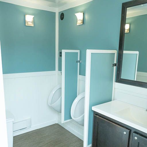 Teal-and-white restroom with two urinals, a sink counter, wall mirror, and bright sconces