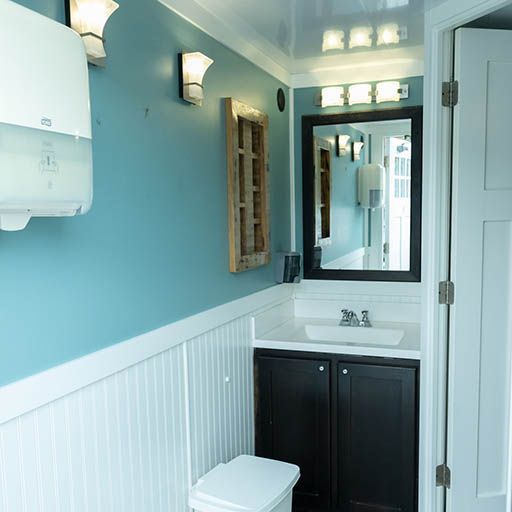 Small bathroom with blue walls, white wainscoting, dark vanity, mirror, sink, and toilet
