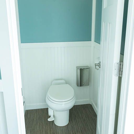 Small bathroom with a white toilet, teal walls, white wainscoting, and a toilet paper dispenser.