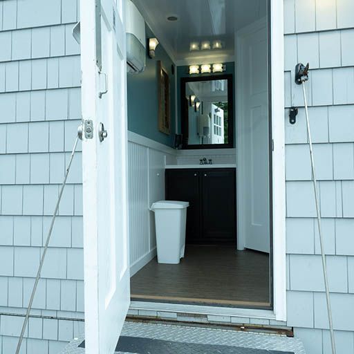 Open front door to a small entryway with a white trash bin and hallway mirror.